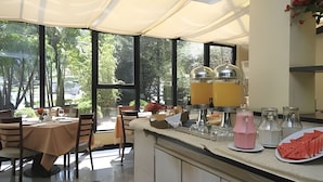 Een moderne keuken met grote ramen, een eethoek met tafels en stoelen, en een aanrecht met keukenapparatuur en een bord eten.