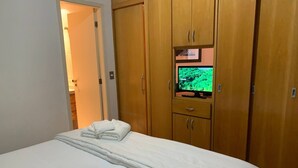 A hotel room with a bed, a television on a wooden cabinet, and a door leading to another room. - Get a Flat 909 Bienal-Ibirapuera  (São Paulo)