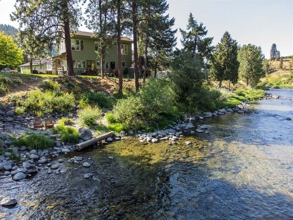A house by a river with a wooden deck and a chair.