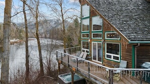 A cabin with a deck, large windows, and a view of a river.
