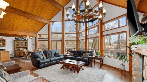 A spacious living room with a high ceiling, large windows, a fireplace, and a chandelier.