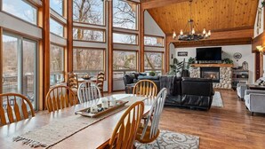 A spacious living area with a fireplace, wooden ceiling, and large windows.