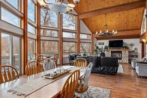 A spacious living area with a fireplace, wooden ceiling, and large windows.
