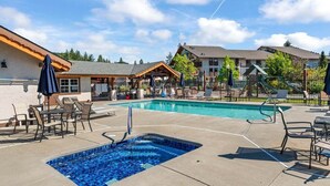 A swimming pool with lounge chairs, a covered seating area, and a building with a sloped roof in the background. - Leavenworth Condo - 1BR w/ Jetted Tub + Pool (Leavenworth)