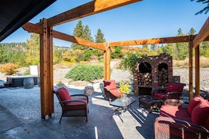A covered outdoor seating area with wicker furniture and a brick fireplace.