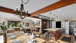 Una cocina amplia con una isla central, vigas de madera y un comedor con una gran mesa dispuesta para seis personas.