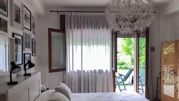 A bedroom with a bed, a desk with two lamps, a large window with curtains, and a view of the outdoors. - Cosy, spacious, bright and central. Three double bedrooms (Venezia)