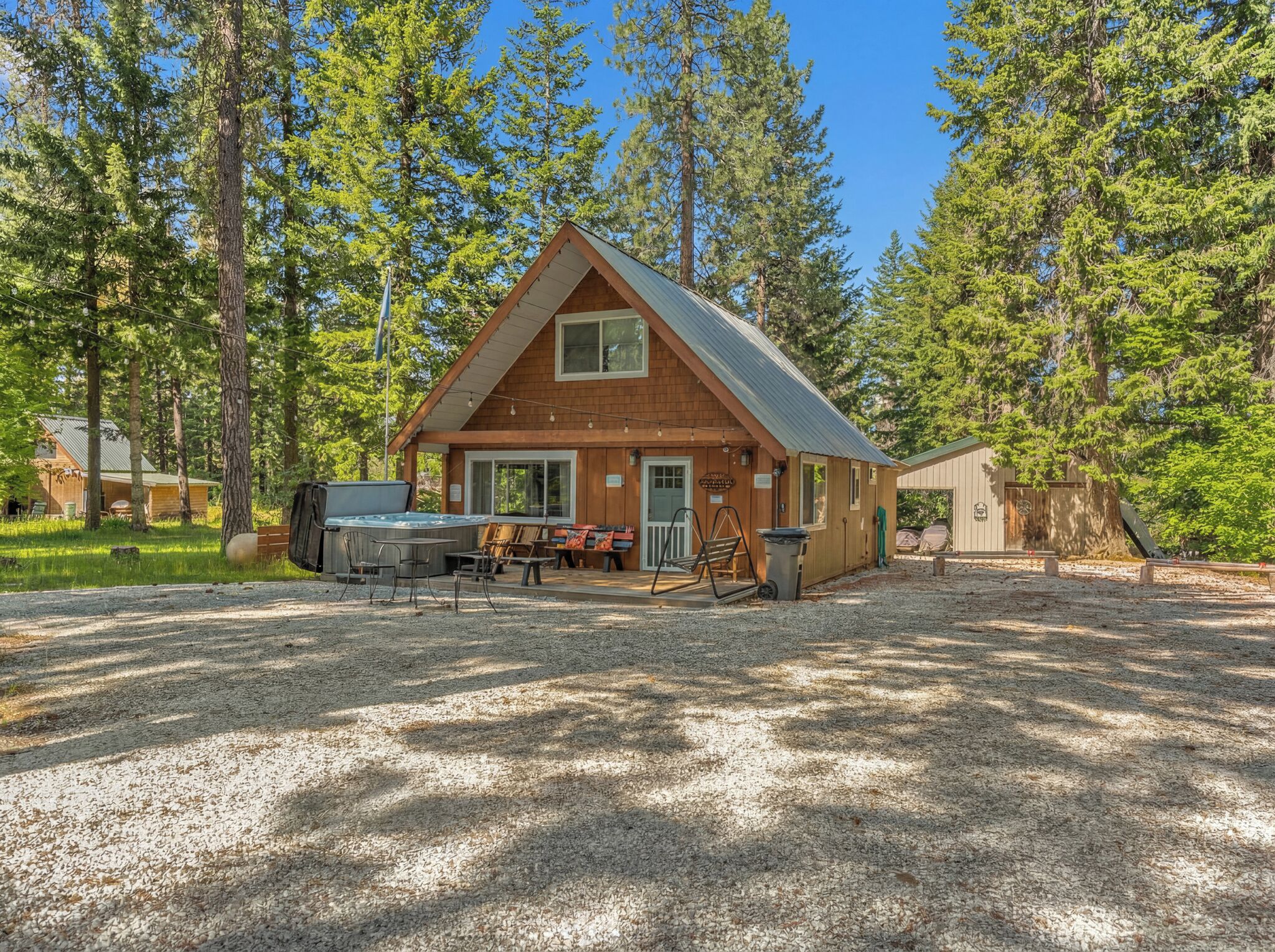 Une cabane en bois dotée d’un bain à remous, d’un espace extérieur aménagé et d’une allée en gravier, le tout entouré d’arbres.