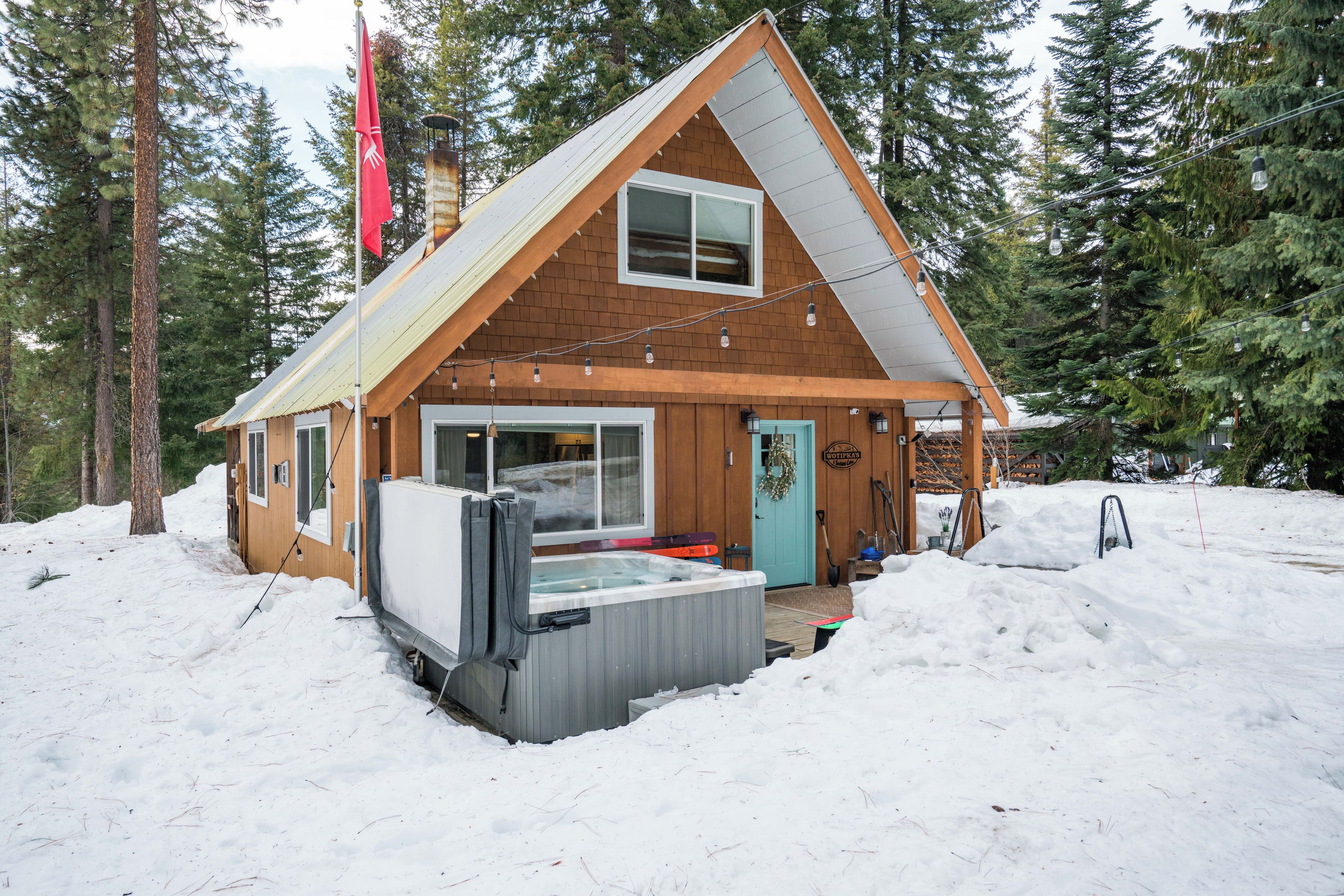 A wooden cabin with a hot tub, surrounded by snow and trees.