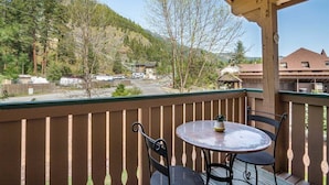 A balcony with a table and chairs, overlooking a mountainous area with sparse trees and buildings in the background.