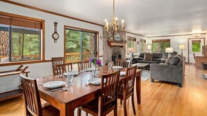 A dining area with a wooden table set for four, surrounded by chairs, a chandelier, and a fireplace. - Buddington Haus - Peaceful nature views (Leavenworth)