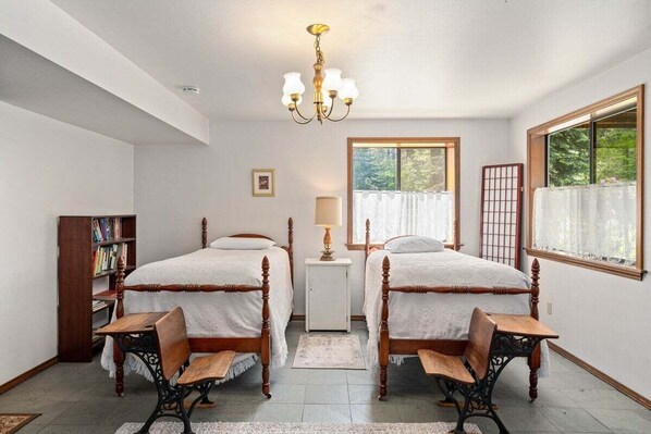 Une chambre à coucher avec deux lits en bois, une table de chevet, une bibliothèque et une fenêtre donnant sur un paysage verdoyant.