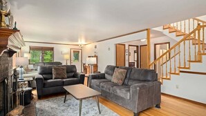 A living room with two sofas, a coffee table, a fireplace, and a staircase. - Buddington Haus - Peaceful nature views (Leavenworth)