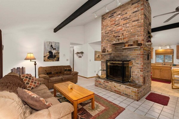 A living room with a brick fireplace, a sofa, a coffee table, and a lamp. - Woodsy Leavenworth Hideaway w/ Hot Tub + Fireplace, Near Trails (Leavenworth)