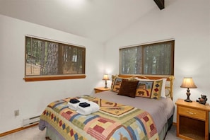 Une chambre à coucher avec un lit, deux tables de chevet avec des lampes et deux fenêtres équipées de stores.