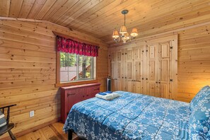 Een houten kamer met een bed, een raam met een rode lambriz en een kledingkast.