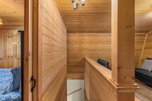 Un intérieur en bois avec un plafond en pente, un lit recouvert d’une courtepointe à motifs floraux bleus et une petite table sur laquelle se trouve un objet noir.