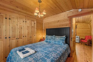 Un dormitori de cabana de fusta amb un llit, una tauleta de nit, una làmpada i una cadira vermella.