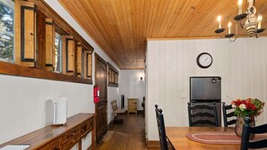 A wooden interior with a dining table, chairs, a clock, and a television.