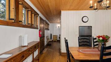 A wooden interior with a dining table, chairs, a clock, and a television.