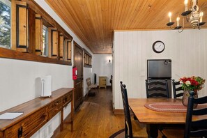 A wooden interior with a dining table, chairs, a clock, and a television.
