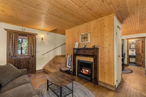 Un salon chaleureux avec une cheminée, des murs en bois, un escalier et un coin repas.