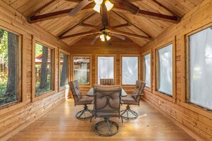 Un intérieur en bois avec une table et des chaises, de grandes fenêtres et un ventilateur de plafond.