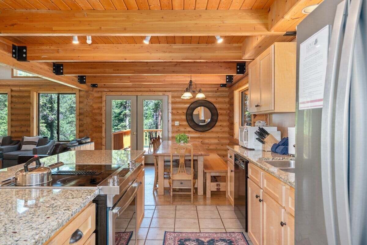Interior de una cabaña de madera con cocina, comedor y sala de estar con sofá y chimenea.