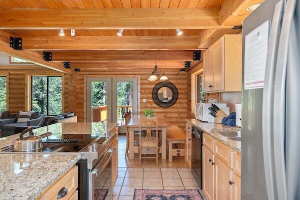 A wooden cabin interior with a kitchen, dining area, and a living room with a sofa and fireplace.