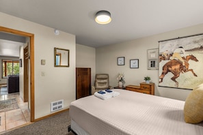 A bedroom with a bed, a chair, a desk, a mirror, and a painting on the wall.