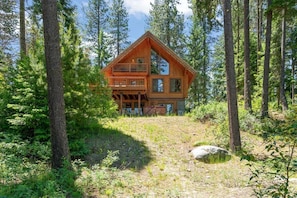 A wooden cabin with a balcony, surrounded by trees.