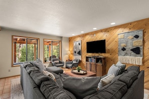 A modern living room with a sectional sofa, two armchairs, a coffee table, and a flat-screen TV mounted on a wooden wall.