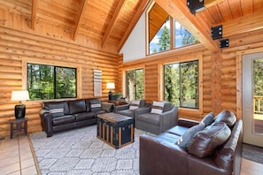 A log cabin interior with a fireplace, large windows, and a cozy seating area.