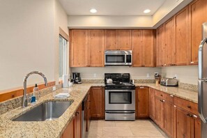 A kitchen with granite countertops, stainless steel appliances, wooden cabinets, and a double sink.