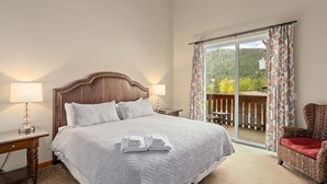 Une chambre avec un grand lit, deux lampes de chevet, un fauteuil et une vue sur un balcon.