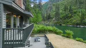 A wooden deck with outdoor furniture, a river view, and a forested hillside. - Riverfront Hot Tub | 4BR Near Leavenworth (Leavenworth)