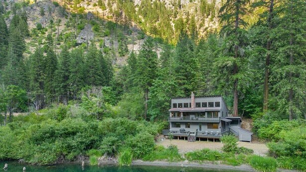 A two-story cabin with a deck, surrounded by dense forest and a lake. - Riverfront Hot Tub | 4BR Near Leavenworth (Leavenworth)