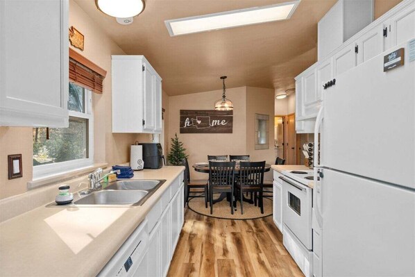 A kitchen with white cabinets, a dining table with chairs, a chandelier, and a 'home' sign on the wall.
