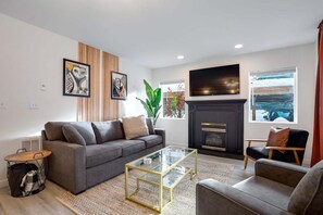 Ein modernes Wohnzimmer mit einer Couch, einem Glastisch, einem Kamin und Kunstwerken an der Wand.