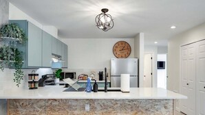 Una cocina moderna con una isla de mármol, taburetes de bar, un reloj y una planta colgante.