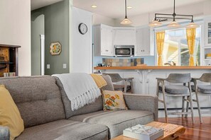 Uma sala de estar moderna com um sofá cinza, uma mesa de centro e uma cozinha com armários brancos e um micro-ondas.