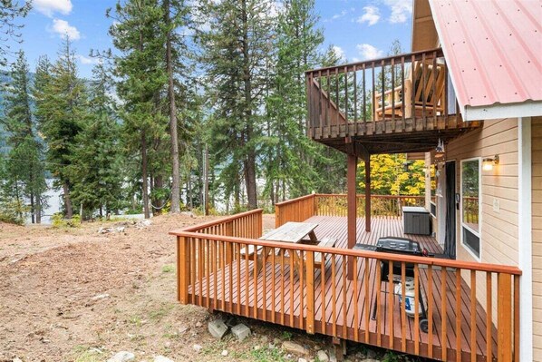 Une cabane dotée d’une terrasse, d’un espace extérieur aménagé et couvert, et offrant une vue sur la forêt environnante.