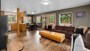 A modern living room with a brown sofa, wooden coffee table, and a kitchen area with wooden cabinets and a dining table. - Pet-Friendly Lake Wenatchee Cabin + Deck (Leavenworth)