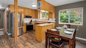 A kitchen with wooden cabinets, stainless steel appliances, a dining area with a table and chairs, and a window with a view of greenery. - Pet-Friendly Lake Wenatchee Cabin + Deck (Leavenworth)