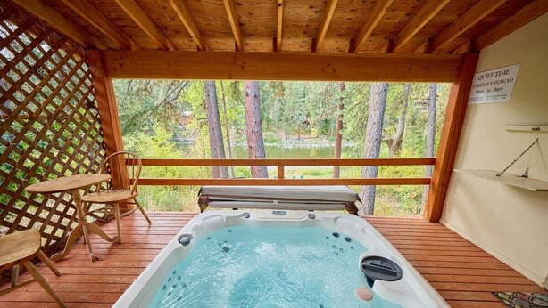 Un jacuzzi en una terraza de madera con vistas a árboles y un cartel que indica horario de silencio.