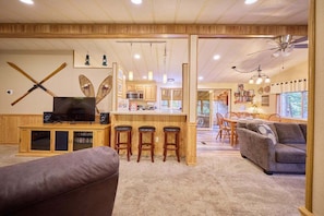 A spacious living room with a large TV, wooden bar area, and a cozy seating arrangement. - Riverfront Family Retreat Near Lake Wenatchee - Screened Porch & Wood Stove (Leavenworth)