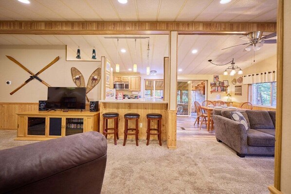 A spacious living room with a large TV, wooden bar area, and a cozy seating arrangement. - Riverfront Family Retreat Near Lake Wenatchee (Leavenworth)