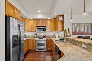 Une cuisine moderne avec des meubles en bois, des appareils en acier inoxydable, des plans de travail en granit et des luminaires suspendus.