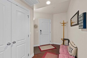 Un couloir avec des portes blanches, un porte-manteau, un paillasson et un coussin sur lequel est écrit le mot «INVITÉ».
