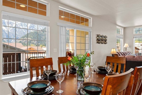A dining area with a table set for four, large windows, and a view of mountains.